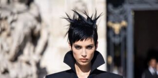 A woman with a dramatic dark rough-cut pixie hairstyle in a tailored suit outside a couture show